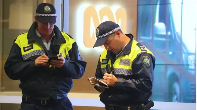 Dua polisi berdiri di depan pintu masuk kantor redaksi ABC di Sydney, Australia.