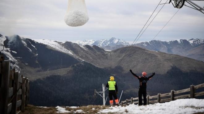 Two men help a helicopter carrying snow near Luchon in French Pyrenees