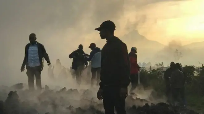 Residents walk near destroyed homes with the smouldering lava deposited by the eruption of Mount Nyiragongo volcano near Goma, in the Democratic Republic of Congo May 23, 2021