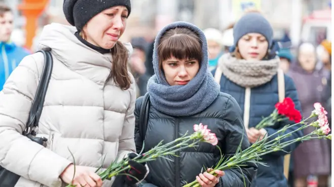 Люди несут цветы к месту пожара