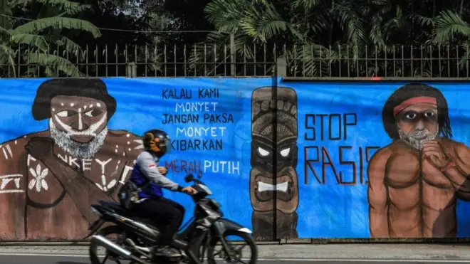Seorang pengendara sepeda motor melewati mural yang menggambarkan kampanye mural menentang rasialisme kepada orang asli Papua.