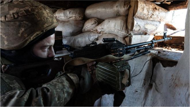 A Ukrainian serviceman points a machine gun through an opening in a sandbag bunker during military exercises