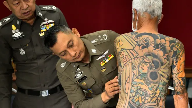 This handout photo taken on January 10, 2018 and received by the Royal Thai Police shows retired Japanese crime boss Shigeharu Shirai (C), 72, being paraded to show his gang-style tattoos to reporters at a police station after his arrest in the central Thai province of Lopburi.