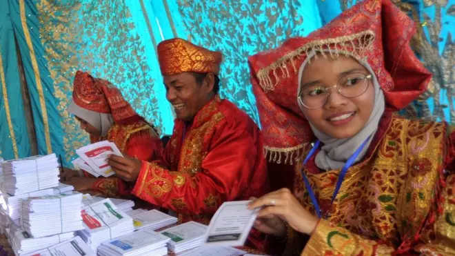 Petugas KPPS mengenakan pakaian pengantin Minang, membagikan surat suara kepada warga saat pemungutan suara Pemilu 2019, di TPS Desa Punggung Ladiang, Pariaman, Sumatera Barat, Rabu (17/04).