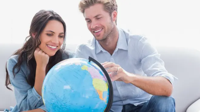 رجل وامرأة ينظرون إلى كرة تمثل الكرة الأرضية وخريطة العالم