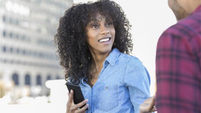 Mujer con un teléfono en la mano se da vuelta para responderle a un desconocido.