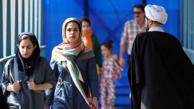 Иранские женщины проходят мимо священнослужителя на улице в Тегеране