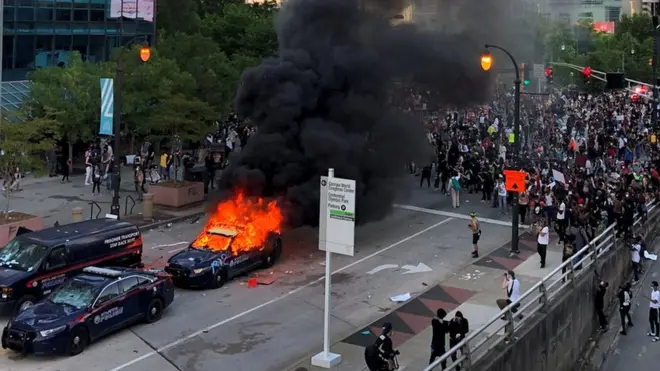 A police car burns as protesters gather near the CNN offices in Atlanta, Georgia