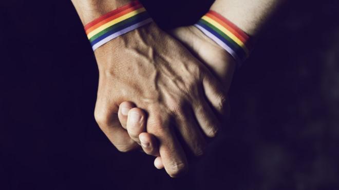 Dos hombres de la mano con cintas multicolores en las muñecas