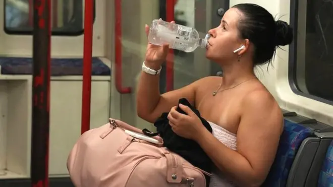 A woman drinks water as she travels on the London Underground during a heatwave