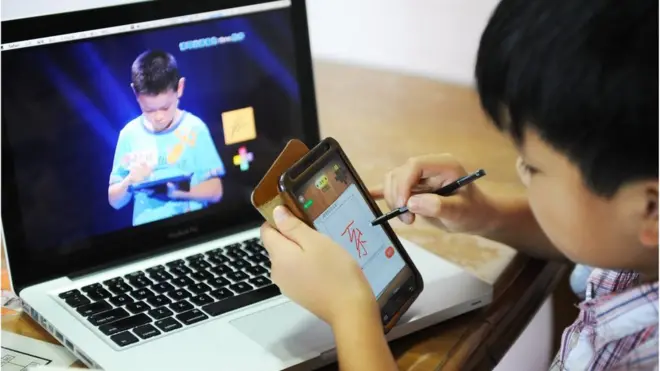 A boy writes a Chinese character on his cellphone as he watches a TV programme called 'hanzi yingxiong', Chinese characters hero, at his home in Beijing on August 23, 2013. AFP PHOTO (Photo credit should read STR/AFP/Getty Images)