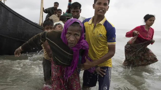 A young Rohingya man carries an elderly woman, after the wooden boat they were travelling on from Myanmar crashed into the shore and tipped everyone out in Dakhinpara, Bangladesh