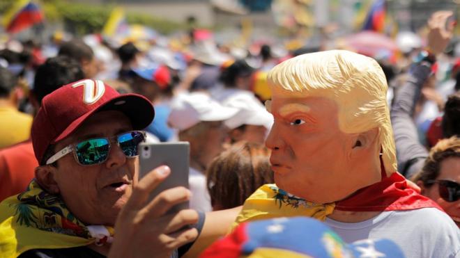A man wearing a mask caricaturing US President Donald Trump poses for a selfie during a rally against Venezuelan President Nicolas Maduro's government in Caracas, February 2, 2019