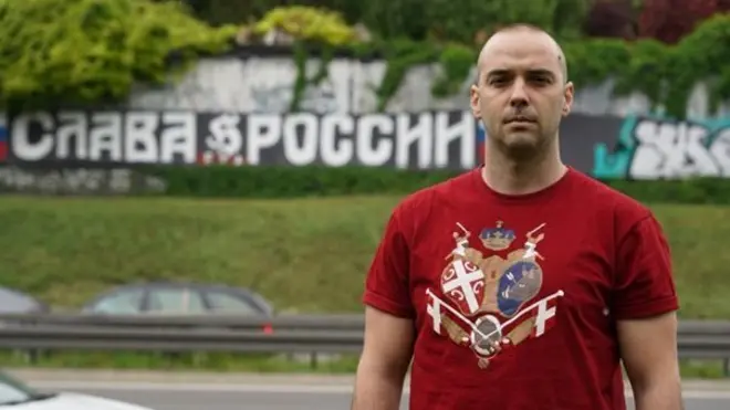 Damjan Knezevic stands in front of a Belgrade street graffiti that reads 'Glory to Russia' in Russian