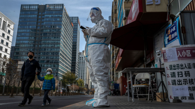 عامل مكافحة الأوبئة يرتدي بدلة واقية يحرس مدخل مبنى سكني مغلق في بكين