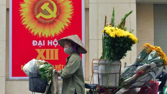 Một phụ nữ bán hàng hoa dắt xe đạp trên một tuyến phố ở Hà Nội hôm 26/01/2021
