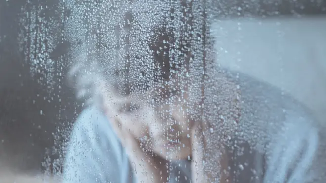Una mujer mira a través de una ventana con lluvia