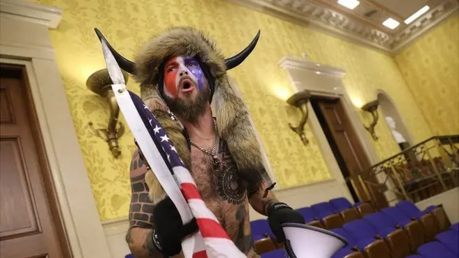 A man in horns and a fur hat, alleged to be Jake Angeli, pictured inside the Senate chamber