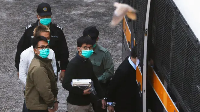 A bird flies in front of pro-democracy activists Ivan Lam and Joshua Wong as they walk to a prison van to head to court, after pleading guilty to charges of organising and inciting an unauthorised assembly near the police headquarters during last year"s anti-government protests, in Hong Kong, China December 2, 2020.