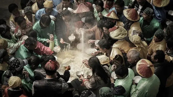 People stand around a giant cauldron eating noodles