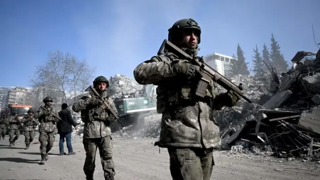 Tentara Turki berpatroli di samping bangunan yang runtuh di Kahramanmaras, 13 Februari 2023.