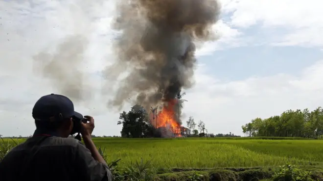 گاوڈو زارا گاؤں میں جلتے ہوئے گاؤں کی تصویر لیتا ایک صحافی