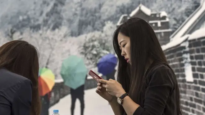 An Asian female participant reads her mobile phone under a poster of the Great Wall of China during the Annual Meeting of the New Champions of the World Economic Forum held in Tianjin from September 18 to 20, 2018. (Photo by Thierry Falise/LightRocket via Getty Images)