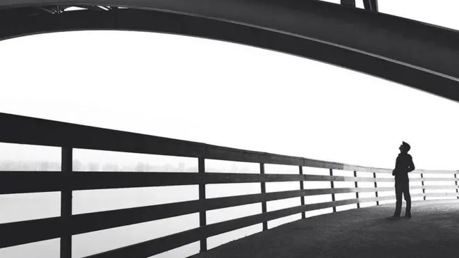 Una persona, a contraluz, caminando por un puente, y mirando a su alrededor, como perdida