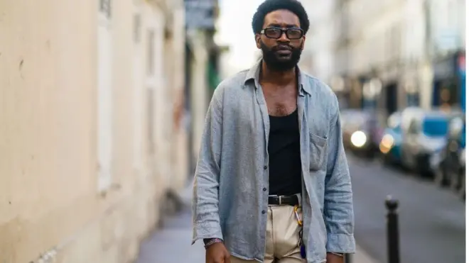 Gali Navangi porte des lunettes de soleil de Port Tanger, une chemise grise vintage, un débardeur noir d'Armani, un pantalon bicolore de Garoze Navangi, une ceinture, le 24 février 2021 à Paris, France.