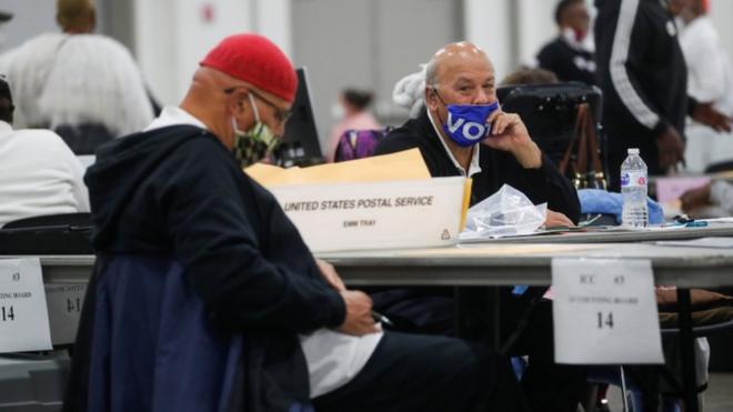 A man wearing a "Vote" mask looks on as votes are counted the day after the 2020 U.S. presidential election, in Detroit, Michigan