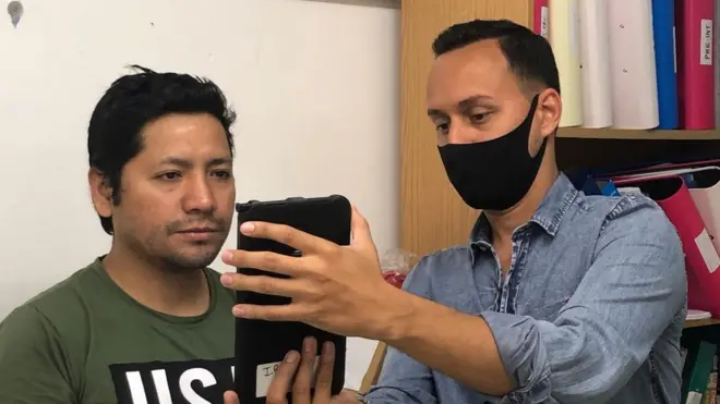 Pedro Manzini, voluntario de IRMO, le saca la foto a Angel Oliver para que, junto con su familia, pueda solicitar la residencia. Crédito: Milli Legrain