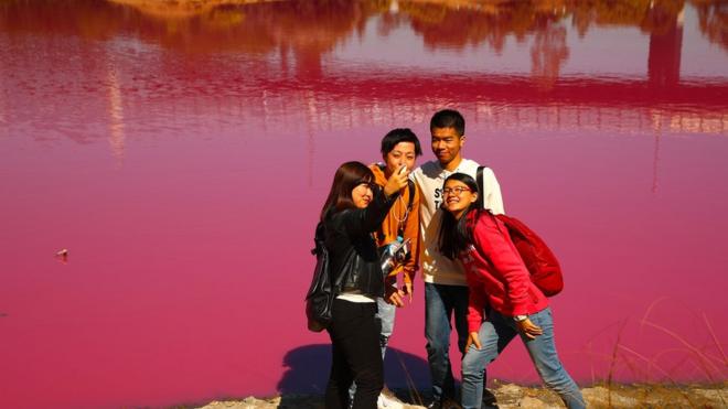 A group of tourists take a selfie in front of the pink lake at Westgate Park