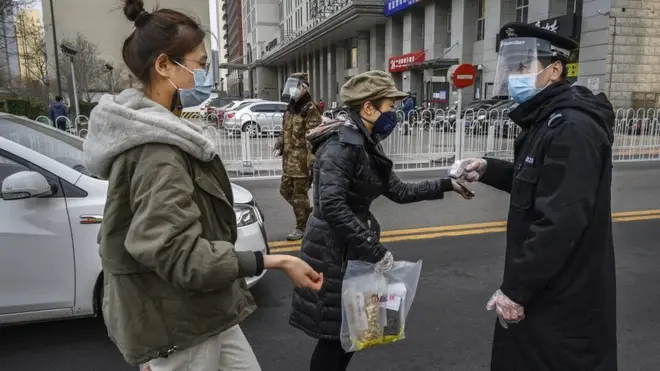 戴上防护面具的一名北京保安在为进入住宅小区的人员测量体温。