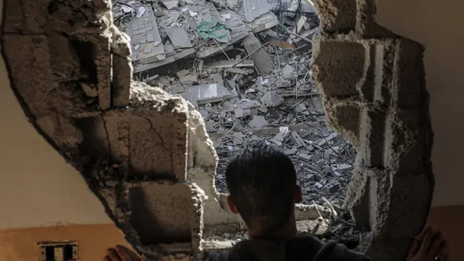 فلسطيني ينظر من داخل منزله الذي تعرض للقصف