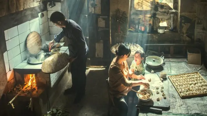Family preparing food indoors, with rays of sunlight shining through the windows
