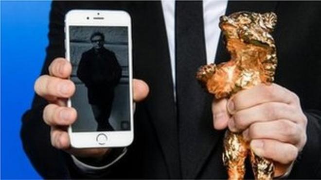 صورة للمخرج محمد رسولوف على هاتف بجانب جائزة "الدب الذهبي"