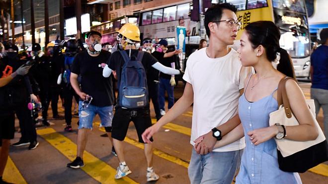 香港尖沙咀一对男女在黑衣示威者中走过（10/8/2019）