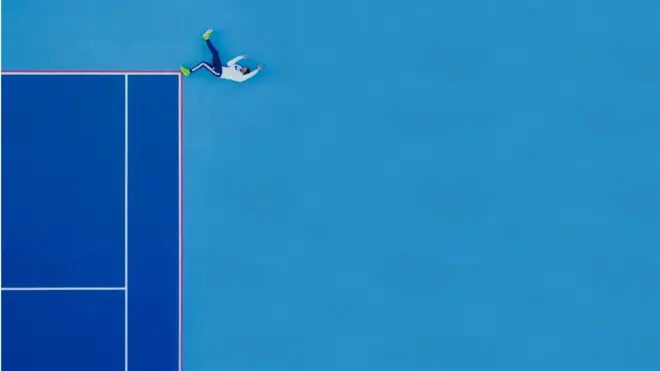 A person poses on the ground at a tennis court.