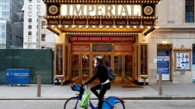 A woman rides a bicycle past the closed Imperial Theatre in Times Square. 12 March 2020
