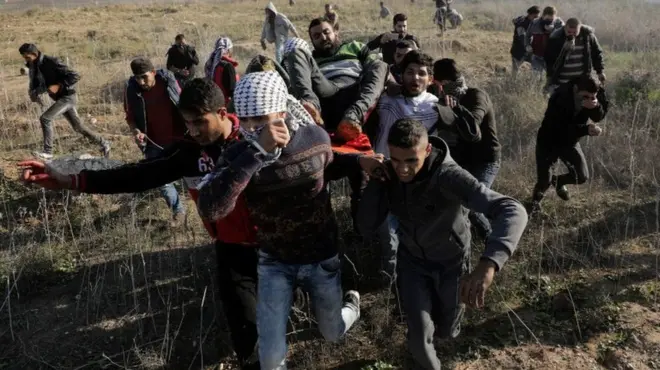 Palestinians carry a wounded protester during clashes along the border between Israel and east Gaza, 8 December 2017
