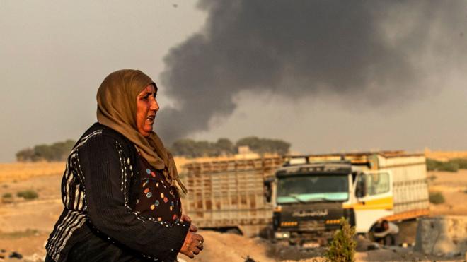 A woman walks as smoke billows following Turkish bombardment in Syria's town of Ras al-Ain