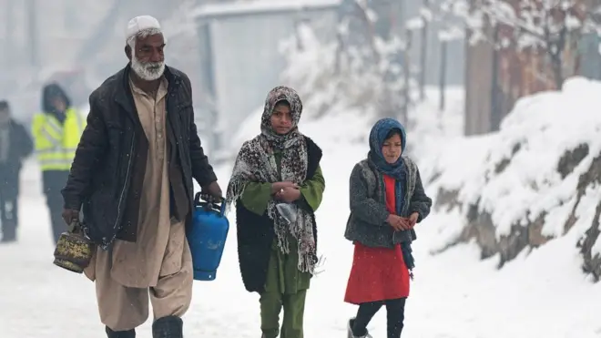 رجل يحمل عبوتا غاز يسير بجوار أطفال على طول أحد الشوارع أثناء تساقط الثلوج في كابل في 11 يناير/كانون الثاني 2023