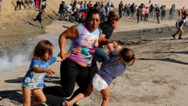 ہونڈورس سے تعلق رکھنے والی ایک پناہ گزین خاتون اپنی پانچ سالہ جوڑواں بچیوں کو آنسو گیس سے بچانے کے لیے بھاگ رہی ہیں۔ یہ واقعہ میکسیکو میں امریکی سرحد کے ساتھ باڑ کے قریب پیش آیا۔