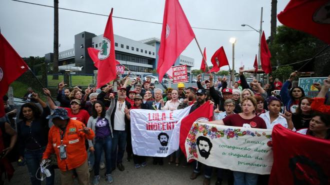 Manifestantes pró-Lula em frente a prédio da Polícia Federal em Curitiba seguram cartazes e bandeiras