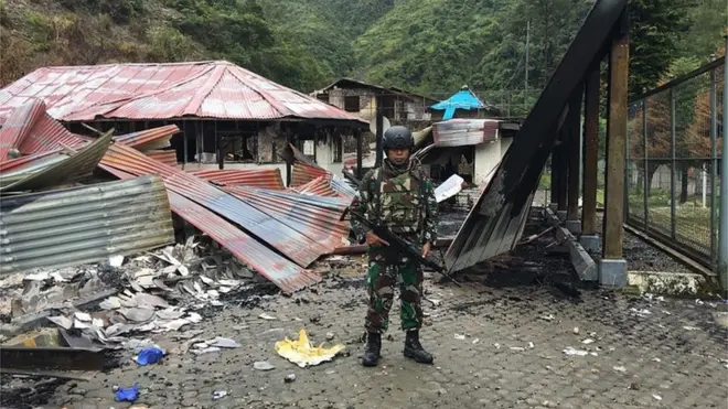 Seorang serdadu dari Kodam Cenderawasih berdiri di sebelah sisa rumah yang terbakar di Tembagapura, Mimika, Papua.