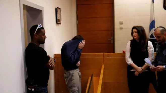 Michael Ron David Kadar (menutup muka) dituduh membuat ratusan ancaman hoax bom.