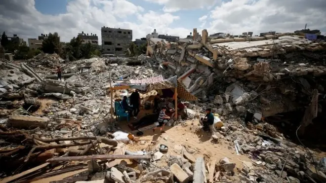 Palestinians sit in a makeshift tent amid the rubble of buildings destroyed in Israeli air strikes in Gaza (23 May 2021)