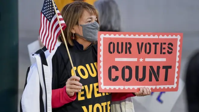 A woman holds an American Flag, and a sign that reads "Our Votes Count". At 5th and Penn Streets in Reading, PA Wednesday evening November 4, 2020 where people gathered to hold a rally to call for all of the votes cast in Tuesday's election to the counted.