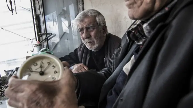 A duo of clock and watch repairmen work in their small metal shop