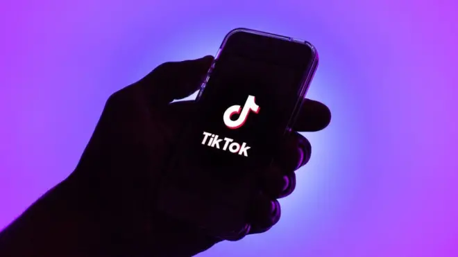 One illustration of hand wey hold phone show di TikTok logo